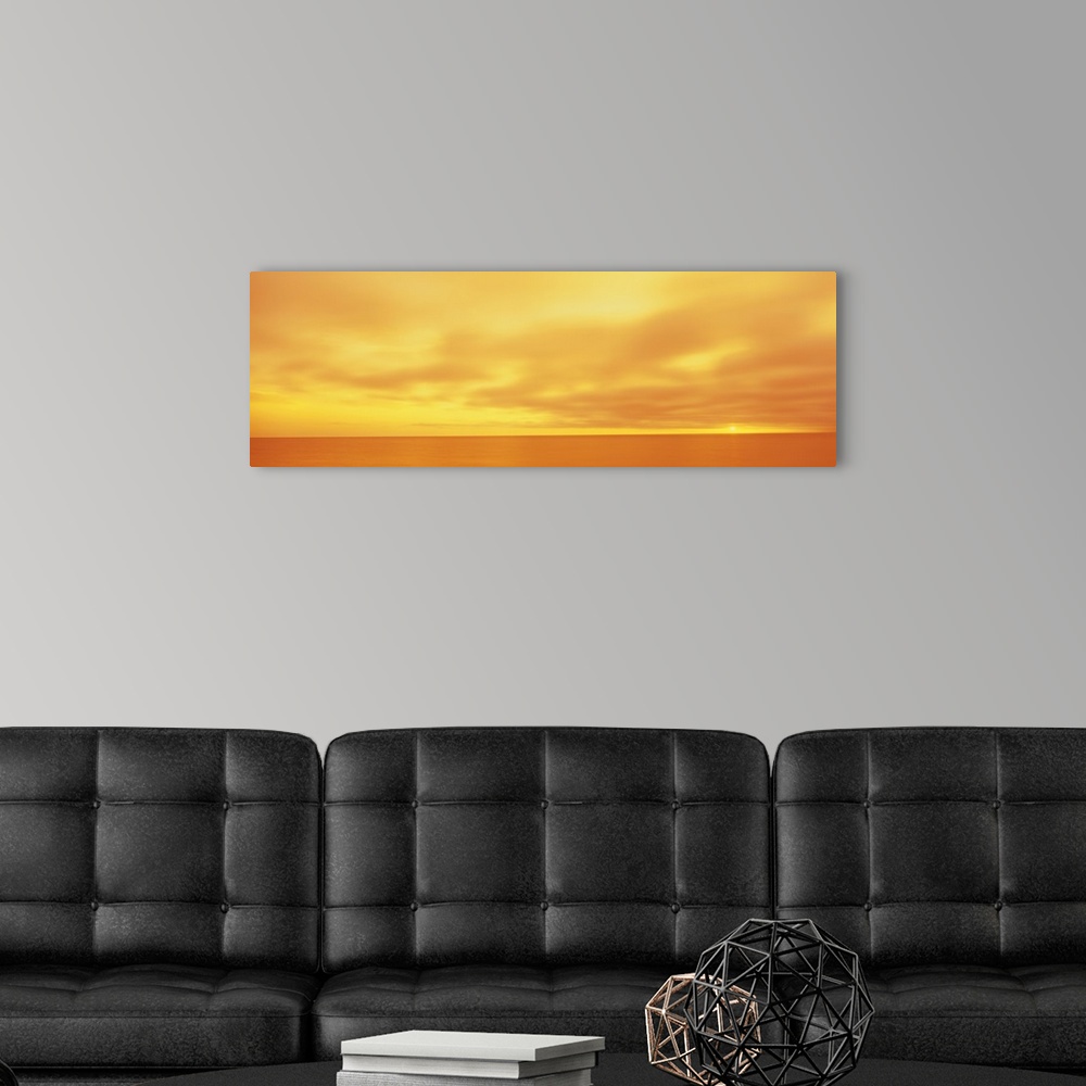 A modern room featuring Panoramic photograph of calm wave less ocean under a cloudy sky.