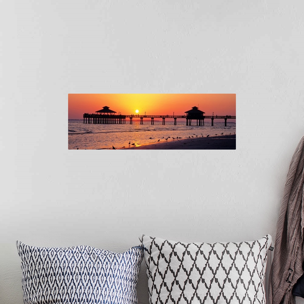 A bohemian room featuring Pier and board walk with shore birds gathered in the foreground as the sun sinks in the sky.