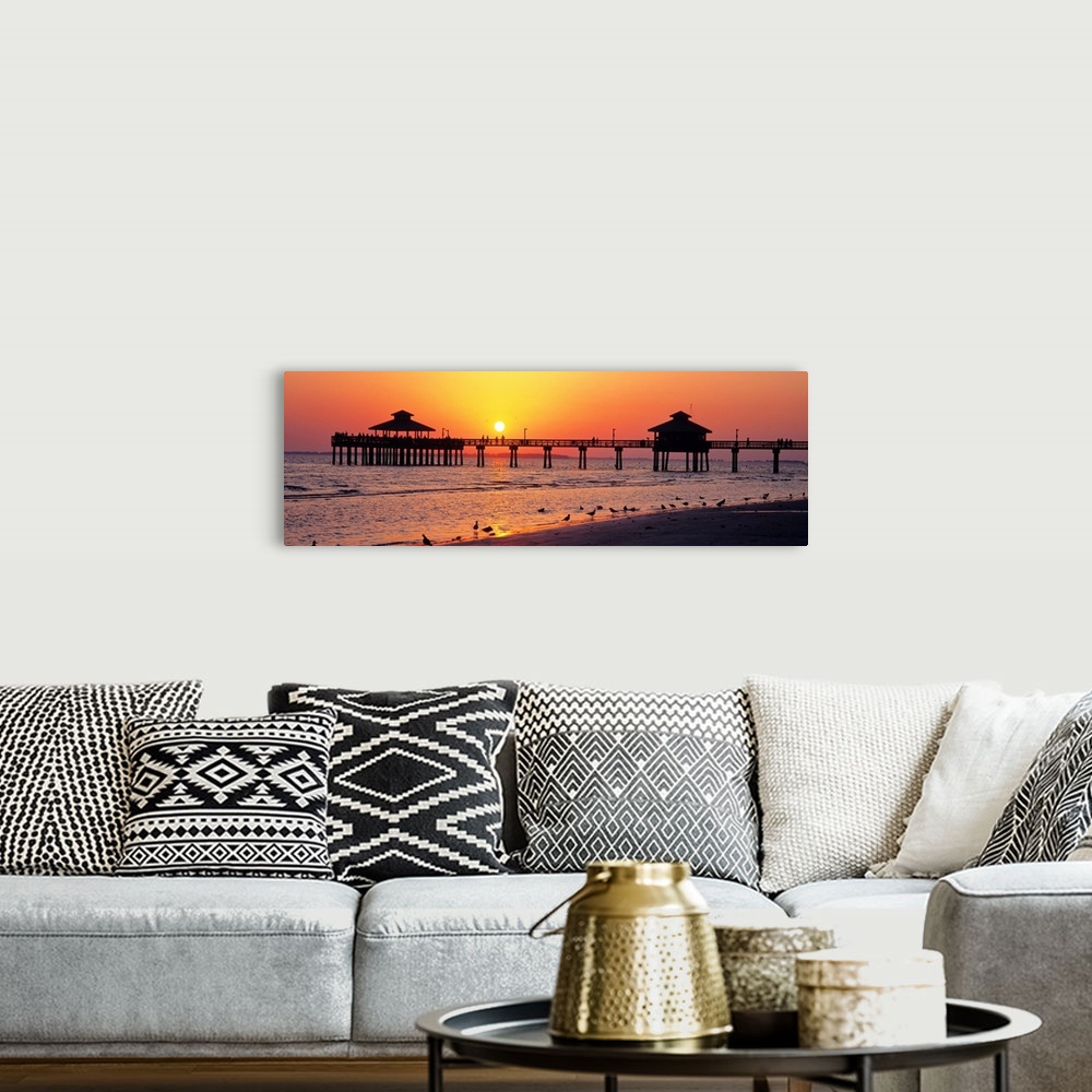 A bohemian room featuring Pier and board walk with shore birds gathered in the foreground as the sun sinks in the sky.