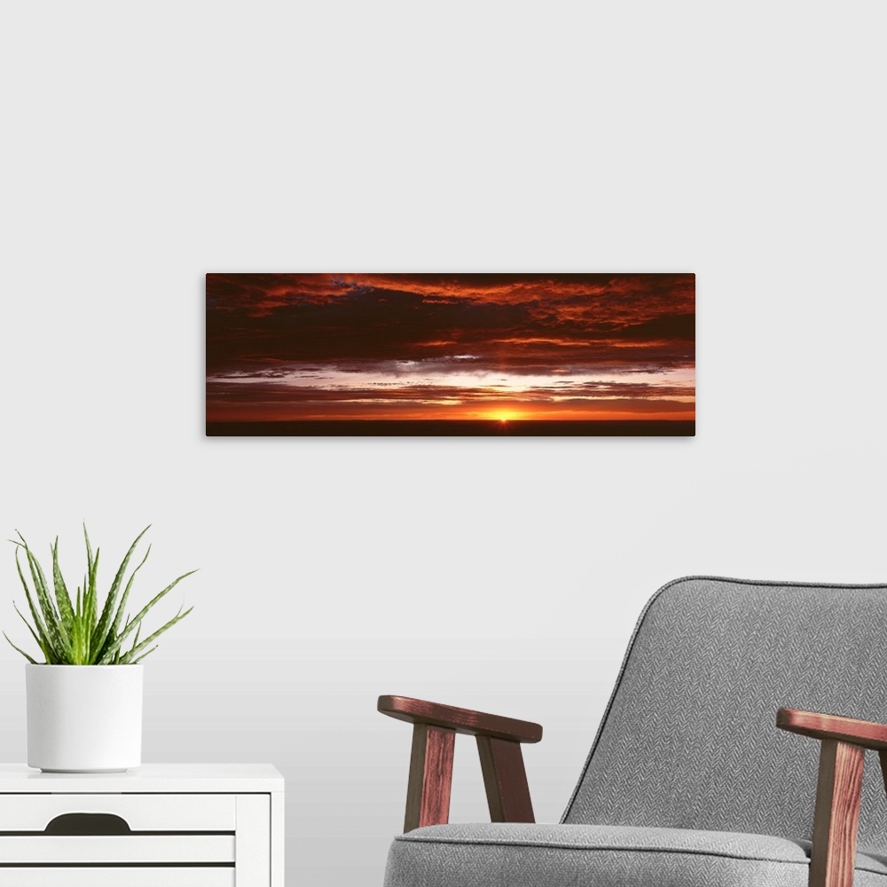 A modern room featuring Panoramic photograph of a sunset just hitting the horizon and lighting up a cloud filled sky with...
