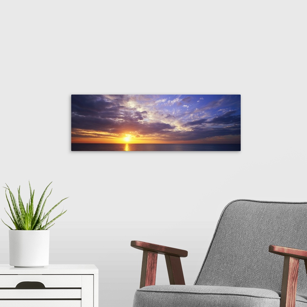 A modern room featuring This large panoramic picture was taken of a sunset about to hit the horizon over the ocean with c...