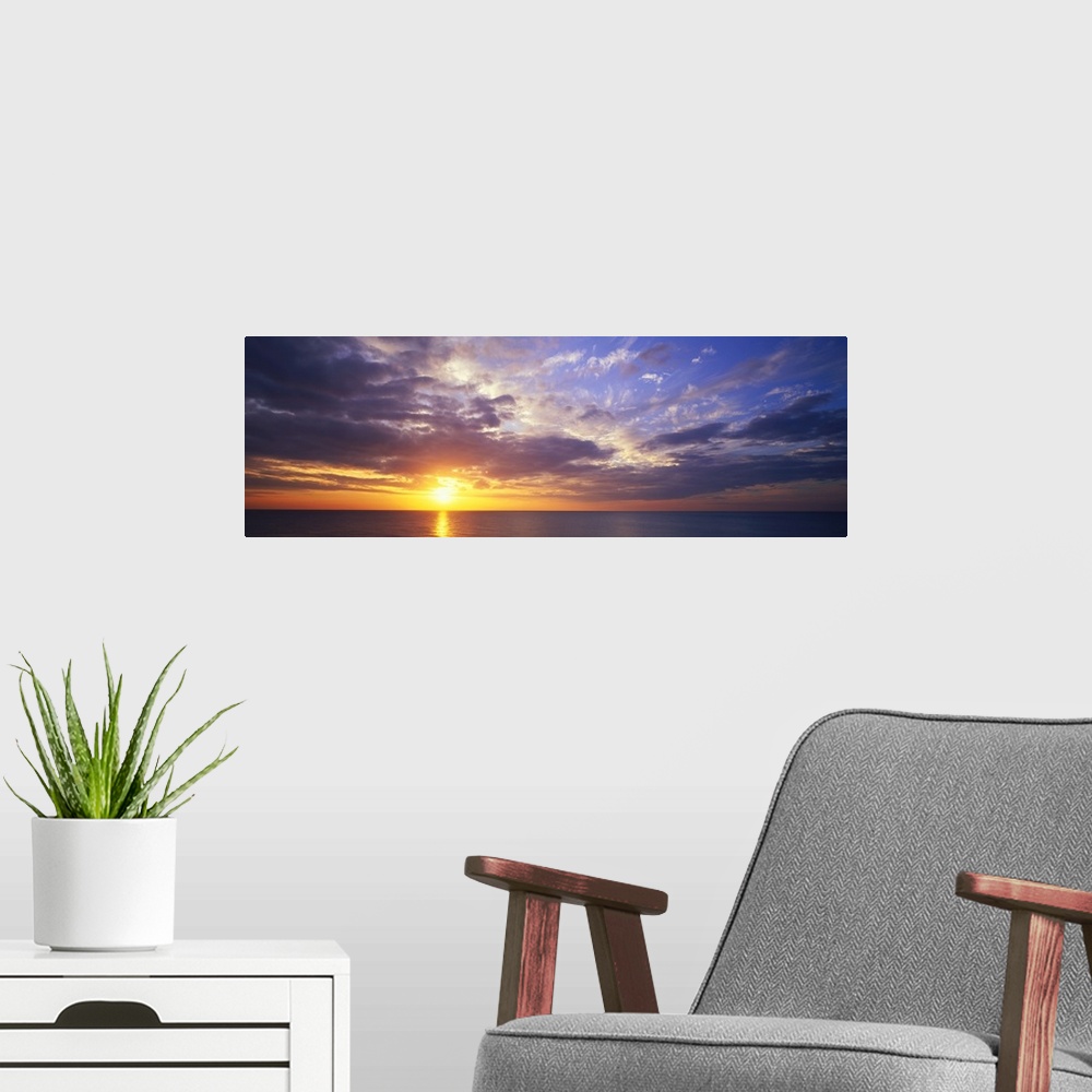 A modern room featuring This large panoramic picture was taken of a sunset about to hit the horizon over the ocean with c...