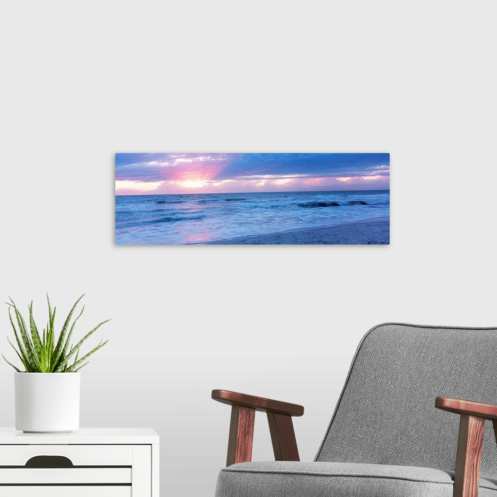 A modern room featuring Large panoramic photo of the sun setting over a beach in Naples, Florida (FL).
