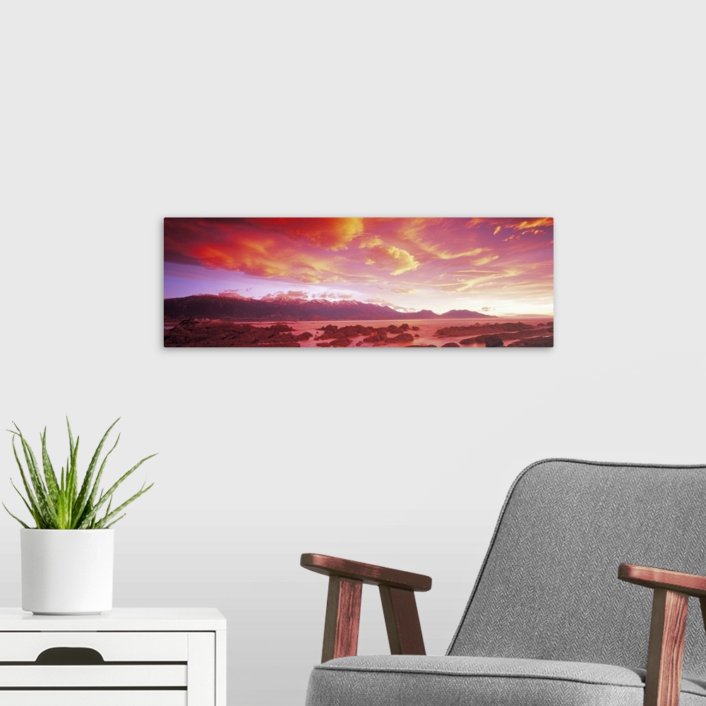 A modern room featuring The sunset paints the sky with warm tones that hang over a mountain range and a body of water.