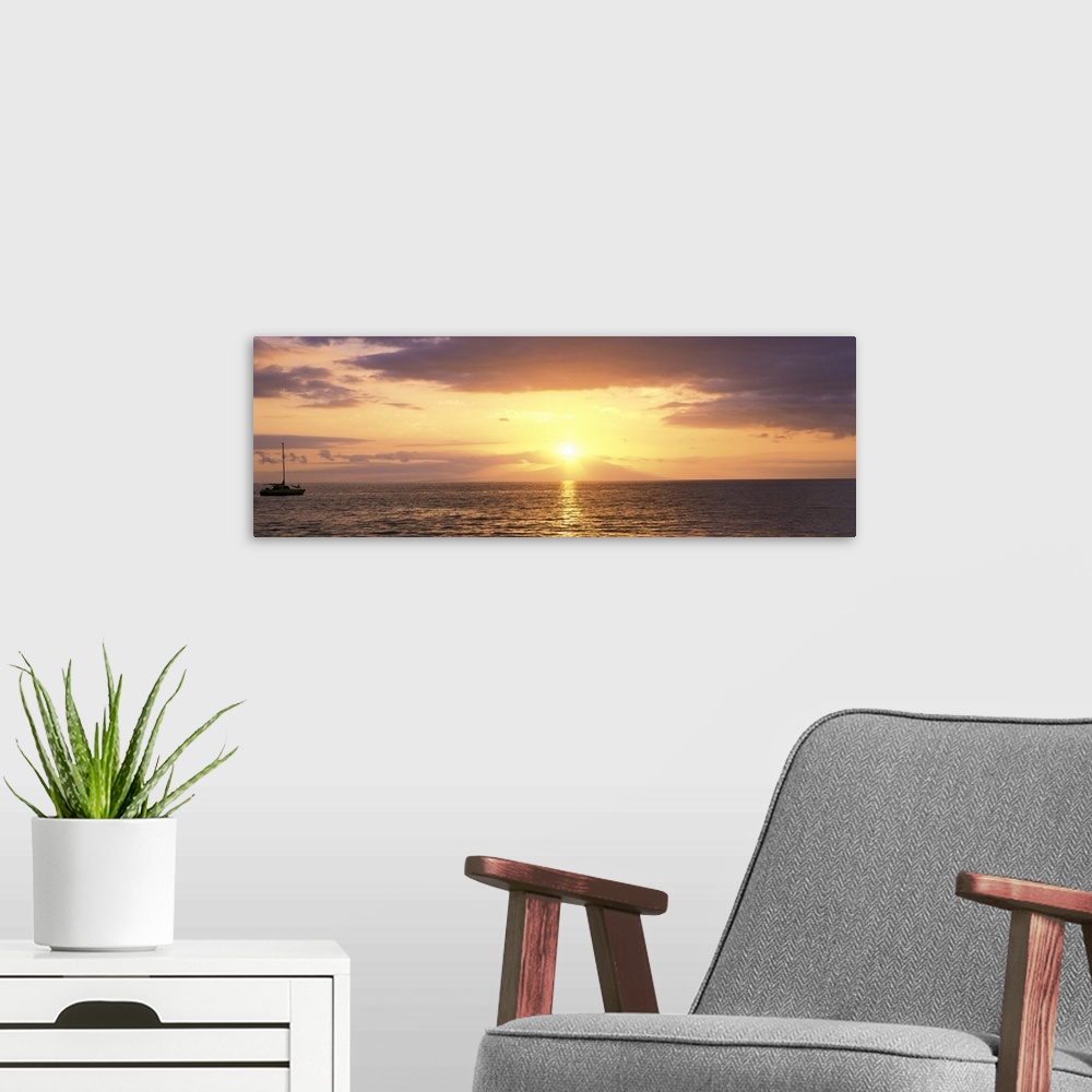 A modern room featuring Panoramic photograph on a large wall hanging of a single boat floating on rippling waters at suns...