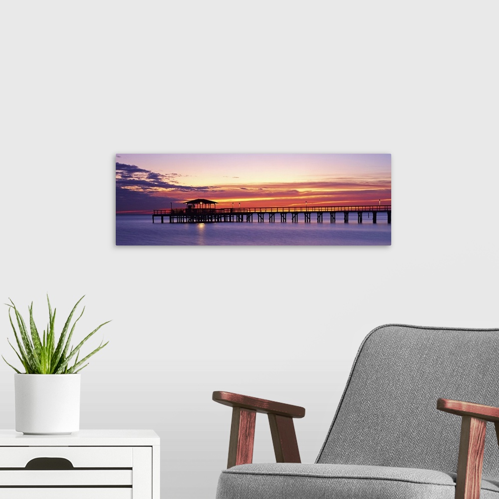 A modern room featuring Wide angle photograph of Mobile Pier surrounded by deep purple waters beneath a vibrant sunset, i...