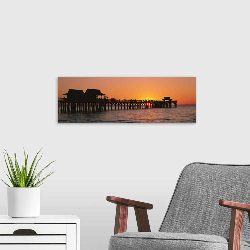 A modern room featuring Panoramic canvas photo art of a silhouetted pier at sunset on the ocean.