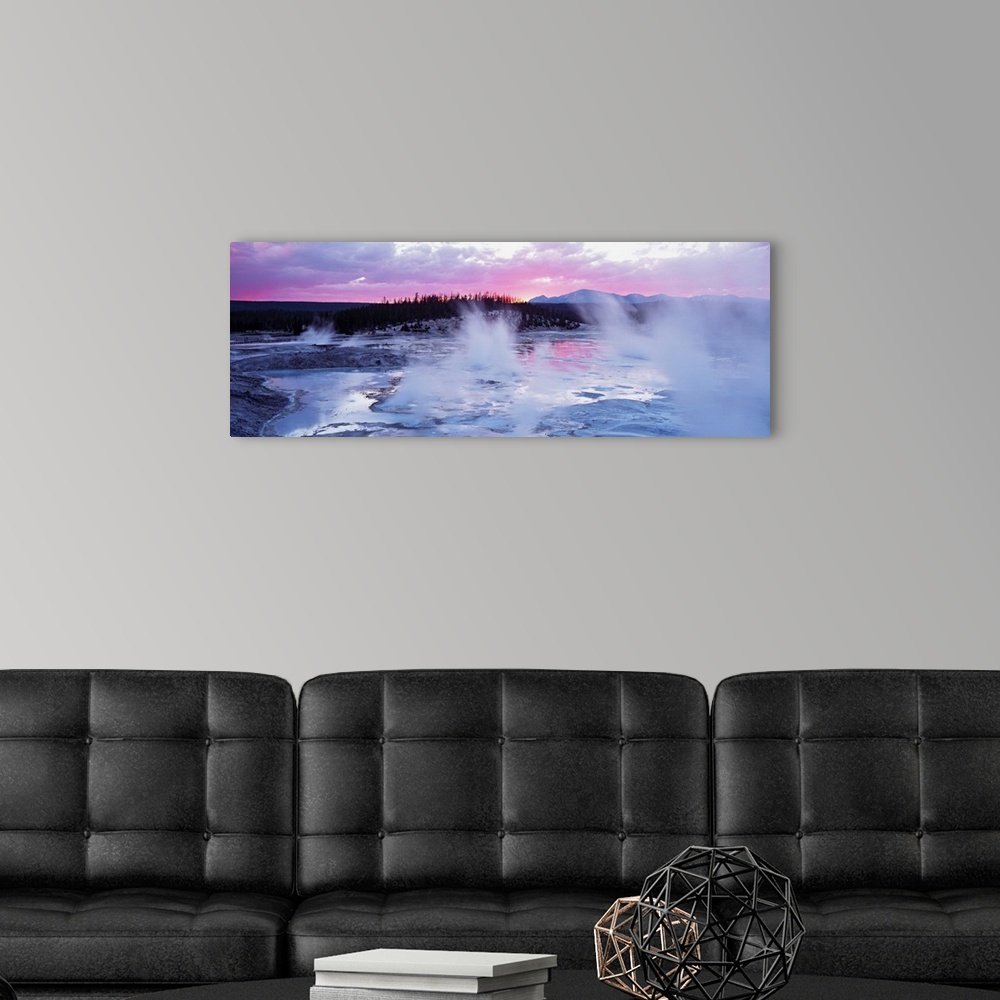 A modern room featuring Large panoramic piece of geysers in Wyoming as the sun sets in the distance and gives the sky pin...