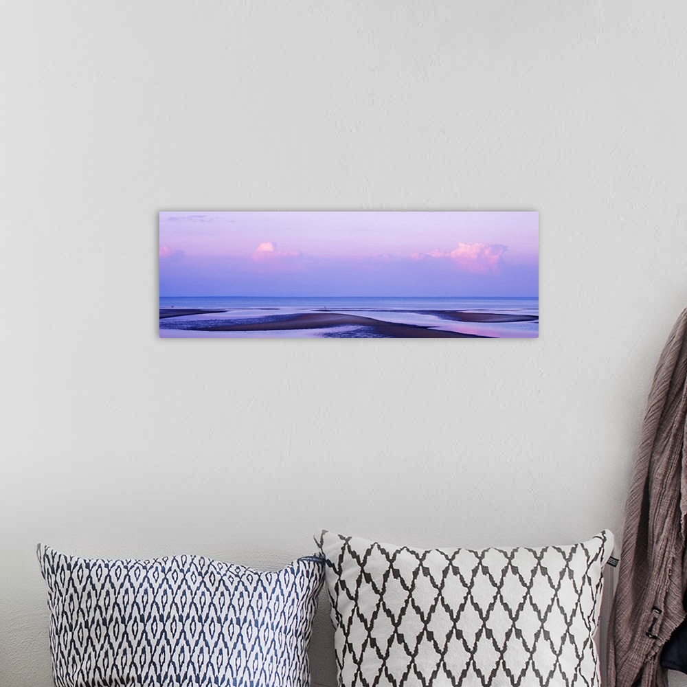 A bohemian room featuring An elongated view of the ocean with large water puddles on the beach and the sky has pink tones f...