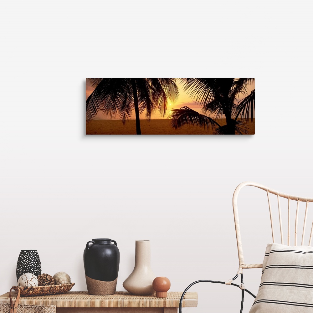 A farmhouse room featuring Silhouettes of palm trees on a beach with the sun sinking below the horizon.