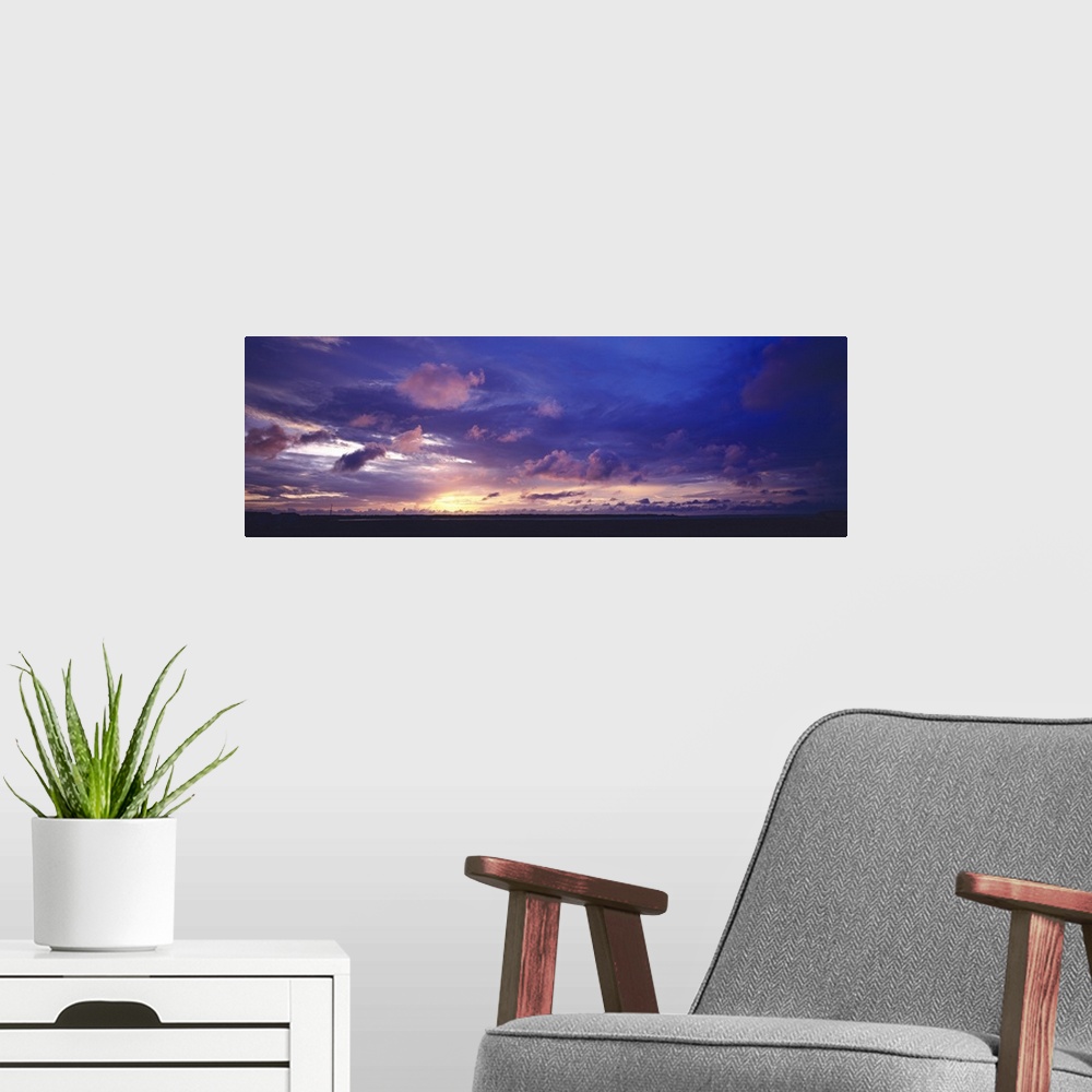 A modern room featuring The sun has set below the horizon but a warm toned sky filled with clouds still hangs over the si...