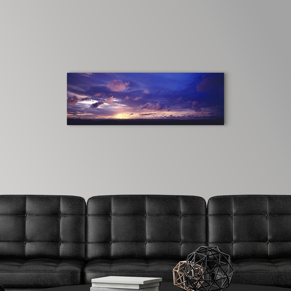 A modern room featuring The sun has set below the horizon but a warm toned sky filled with clouds still hangs over the si...