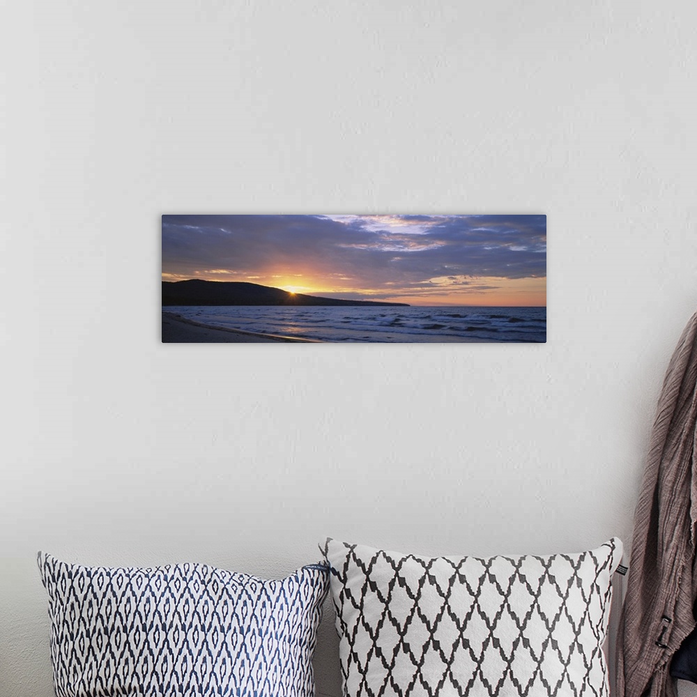A bohemian room featuring Panoramic canvas photo of waves crashing in the ocean and a setting sun peeking through a rolling...