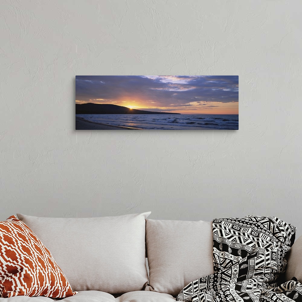 A bohemian room featuring Panoramic canvas photo of waves crashing in the ocean and a setting sun peeking through a rolling...