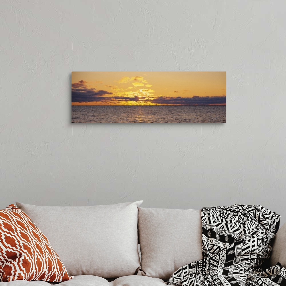 A bohemian room featuring Panoramic photo on canvas of a sunset shining through clouds above a lake.