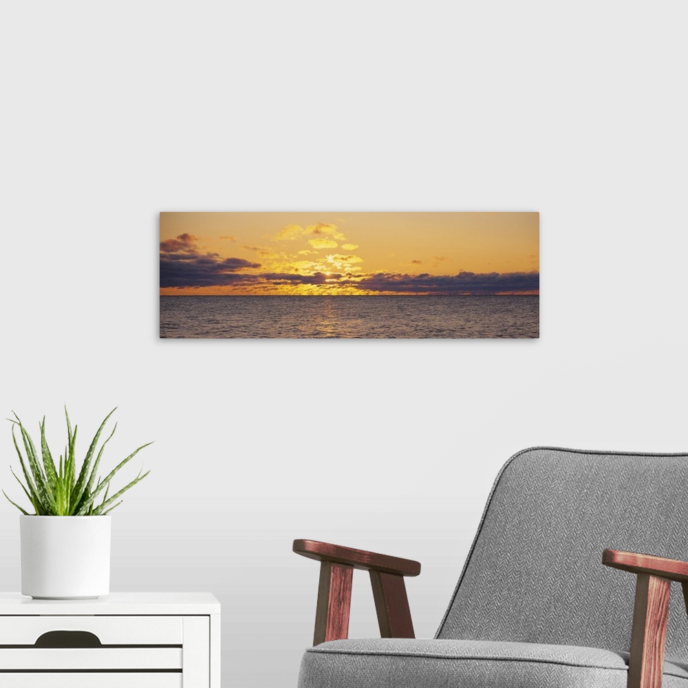A modern room featuring Panoramic photo on canvas of a sunset shining through clouds above a lake.