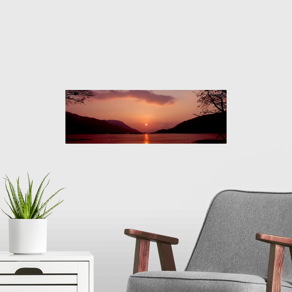 A modern room featuring Panoramic photo on canvas of a sunset over the water with rolling hills in the background.
