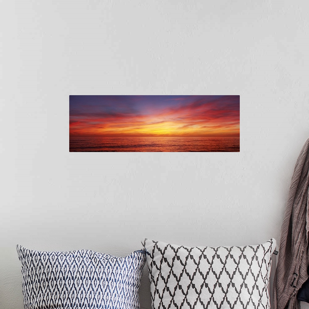 A bohemian room featuring A panoramic photograph of the sun descending behind clouds over the ocean.