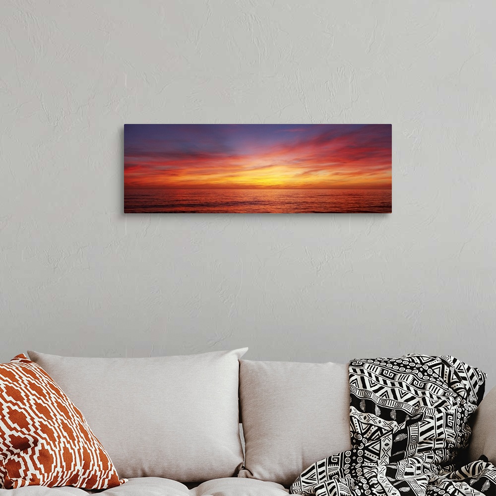 A bohemian room featuring A panoramic photograph of the sun descending behind clouds over the ocean.