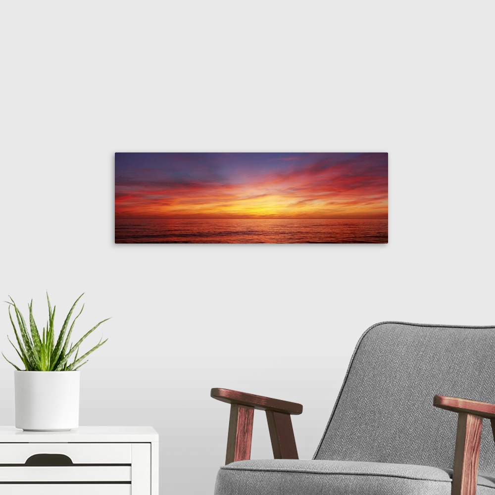 A modern room featuring A panoramic photograph of the sun descending behind clouds over the ocean.