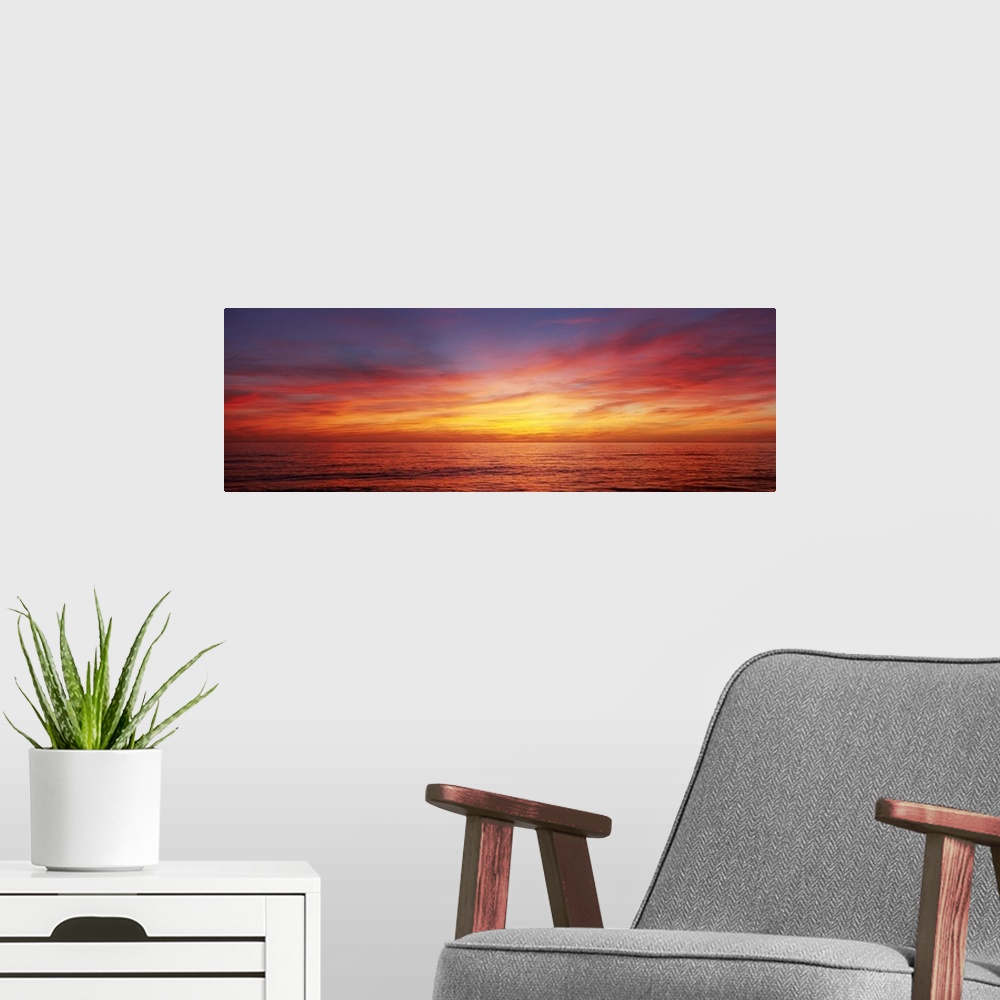 A modern room featuring A panoramic photograph of the sun descending behind clouds over the ocean.