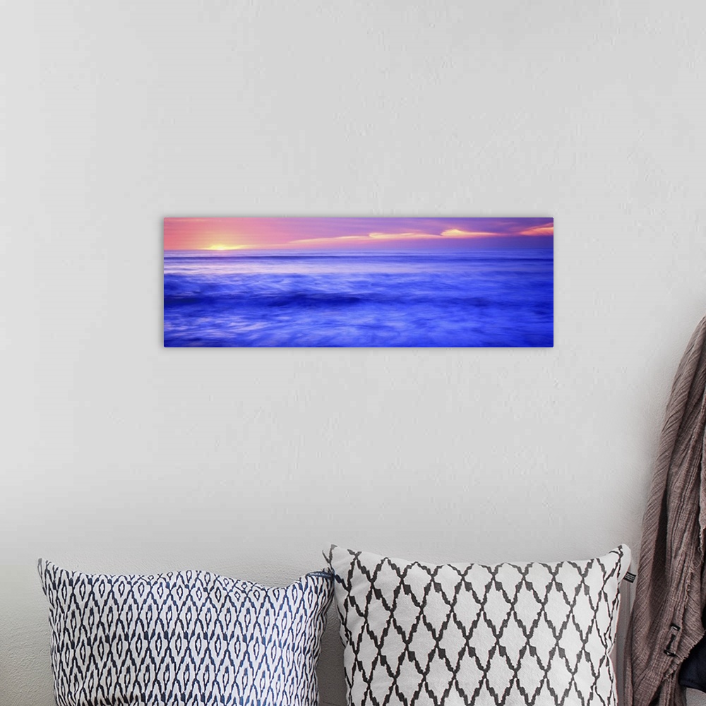 A bohemian room featuring Panoramic photograph shows the sun setting over the horizon and sparkling over a coast of the Wes...