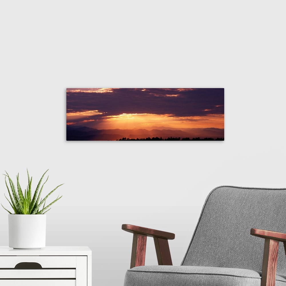 A modern room featuring Wide angle photograph of the sun setting behind a cloudy sky, over the distant Rocky Mountains.  ...
