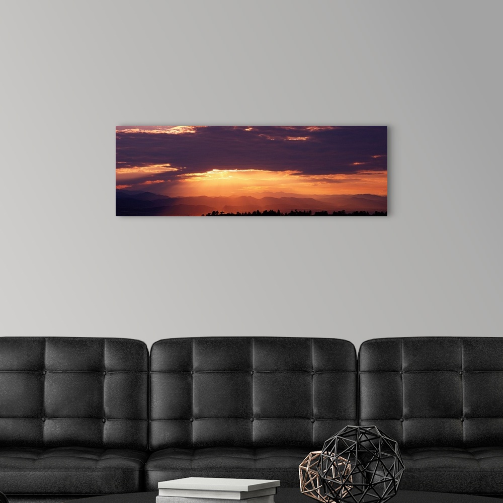 A modern room featuring Wide angle photograph of the sun setting behind a cloudy sky, over the distant Rocky Mountains.  ...