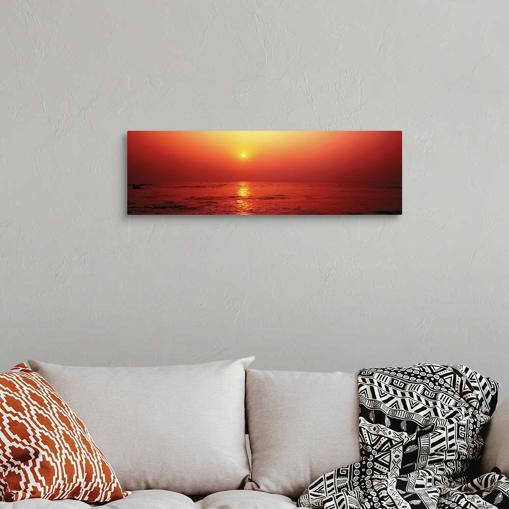 A bohemian room featuring Panoramic photograph taken of the sun as it begins to set in the sky. The entire picture has a wa...