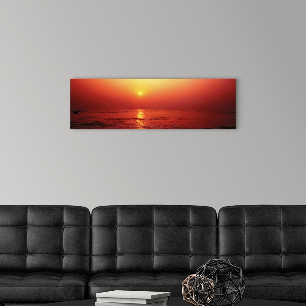 A modern room featuring Panoramic photograph taken of the sun as it begins to set in the sky. The entire picture has a wa...