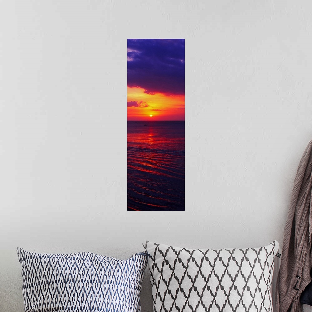 A bohemian room featuring Vertical, large photograph of the sun setting in a vibrant, fiery sky over dark ocean waters, nea...