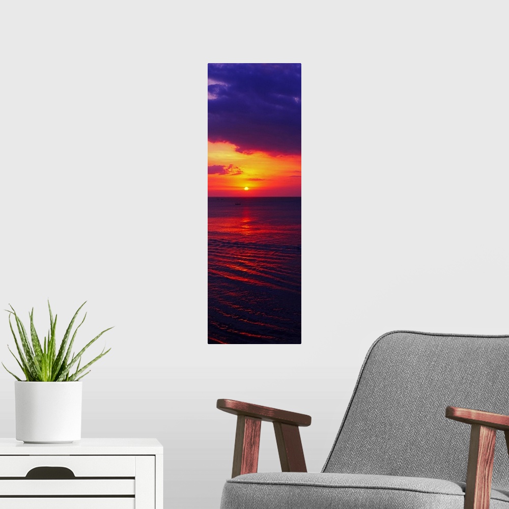 A modern room featuring Vertical, large photograph of the sun setting in a vibrant, fiery sky over dark ocean waters, nea...