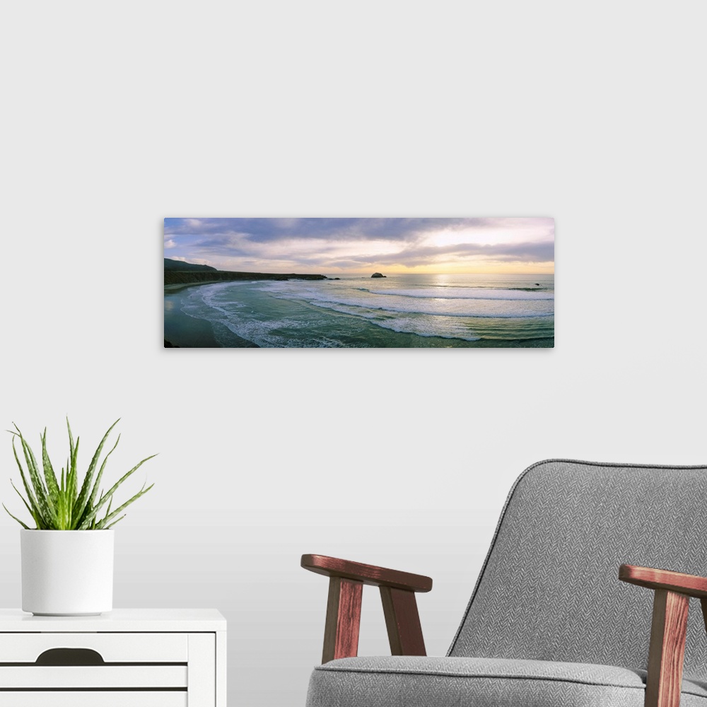 A modern room featuring This panoramic wall art is a wide angle photograph of waves washing on to a beach taken from a cl...
