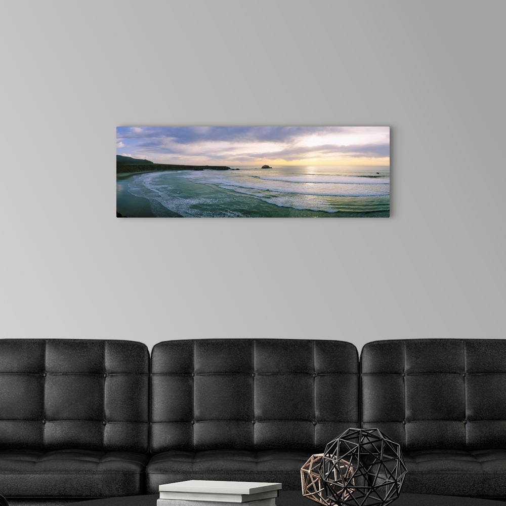 A modern room featuring This panoramic wall art is a wide angle photograph of waves washing on to a beach taken from a cl...