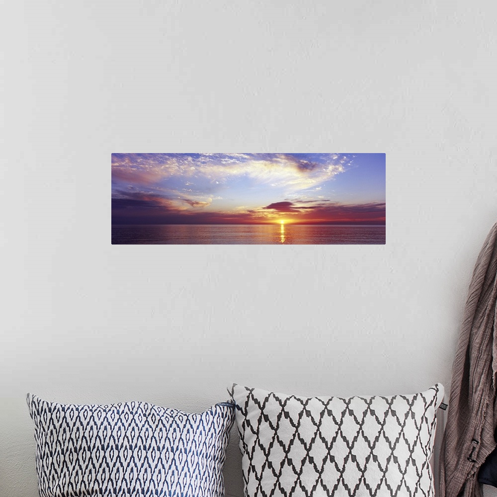 A bohemian room featuring Large panoramic photograph of a sunset over the ocean with a cloud filled sky.