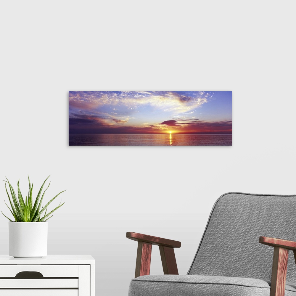 A modern room featuring Large panoramic photograph of a sunset over the ocean with a cloud filled sky.