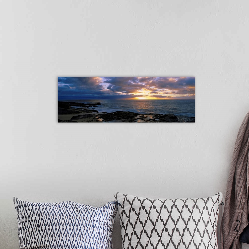 A bohemian room featuring A panoramic photograph of the sun setting beyond the horizon as viewed from a rocky tropical beach.