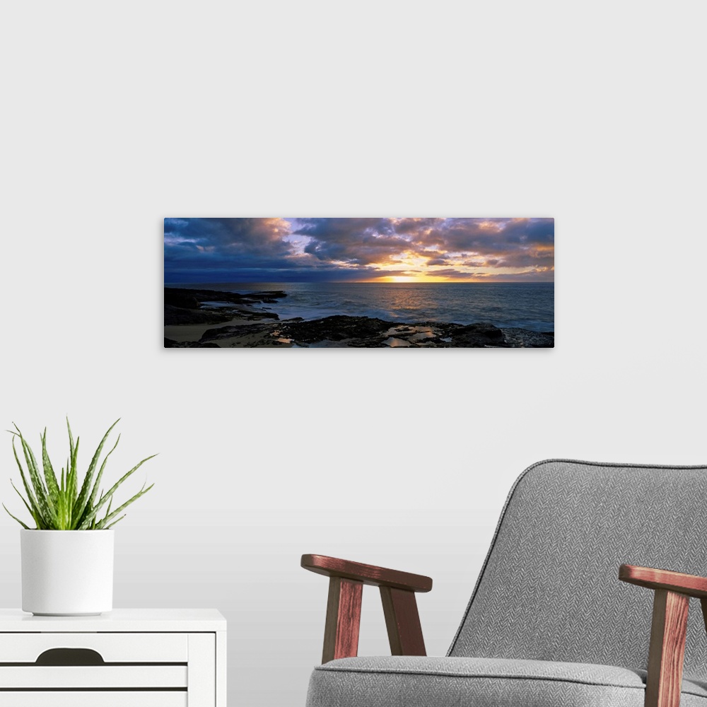 A modern room featuring A panoramic photograph of the sun setting beyond the horizon as viewed from a rocky tropical beach.