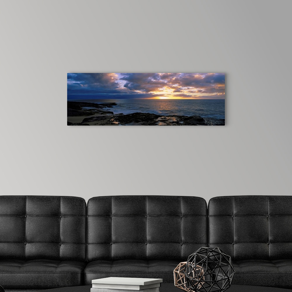 A modern room featuring A panoramic photograph of the sun setting beyond the horizon as viewed from a rocky tropical beach.