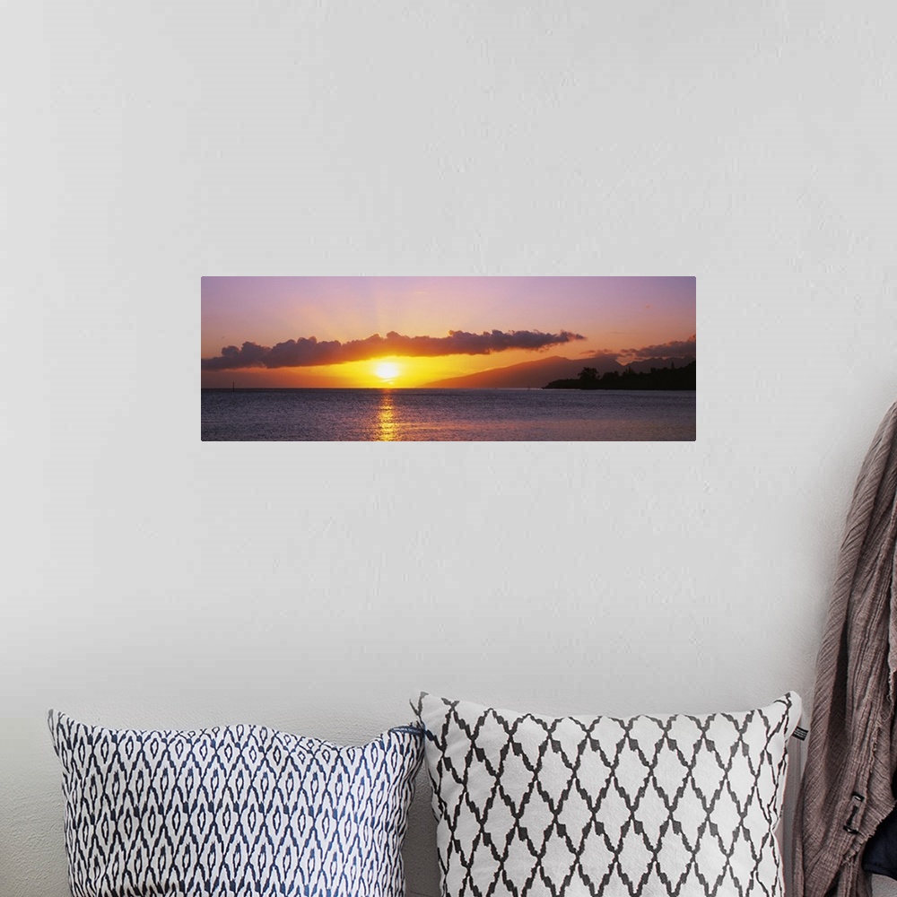 A bohemian room featuring Panoramic photograph of sun and clouds over ocean at dusk.