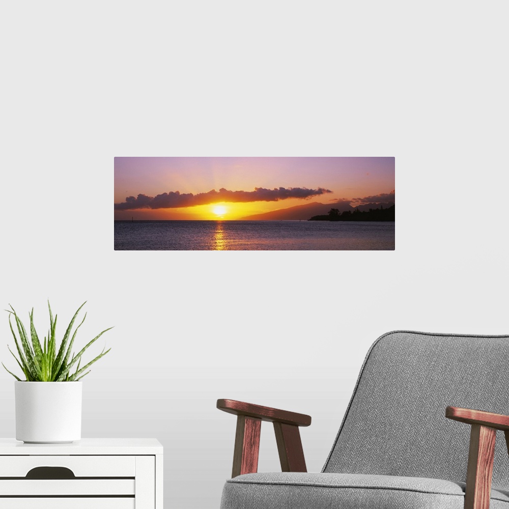 A modern room featuring Panoramic photograph of sun and clouds over ocean at dusk.