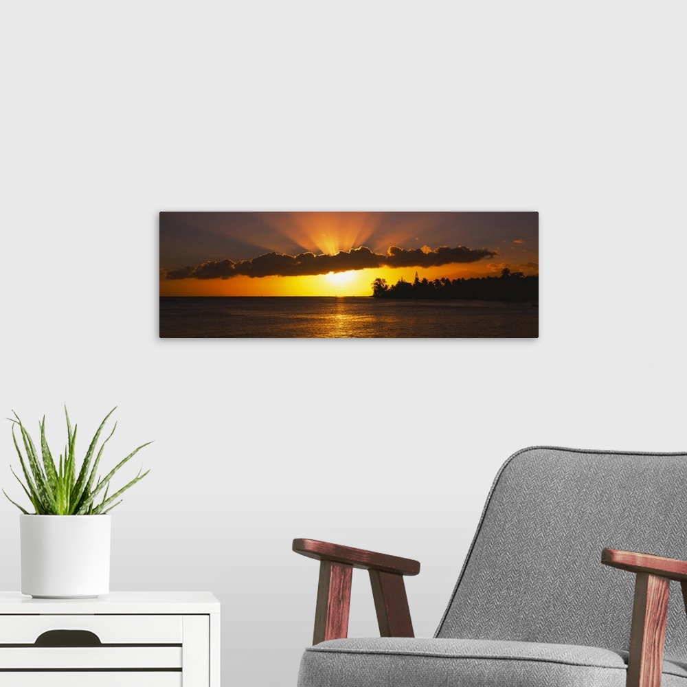 A modern room featuring Panoramic photograph of the sun setting behind the clouds over the water in Tahiti.