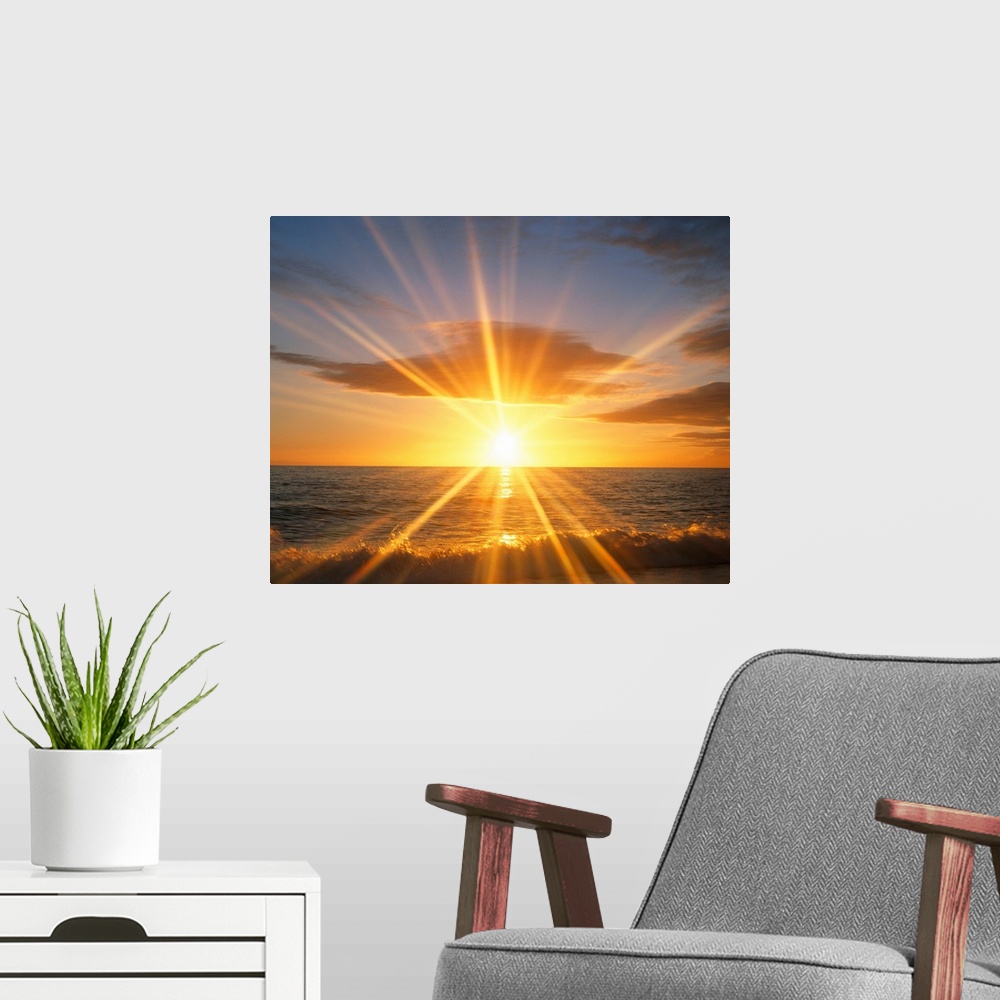 A modern room featuring Giant photograph of a bright sunset reflecting onto an ocean as the waves crash against a sandy b...