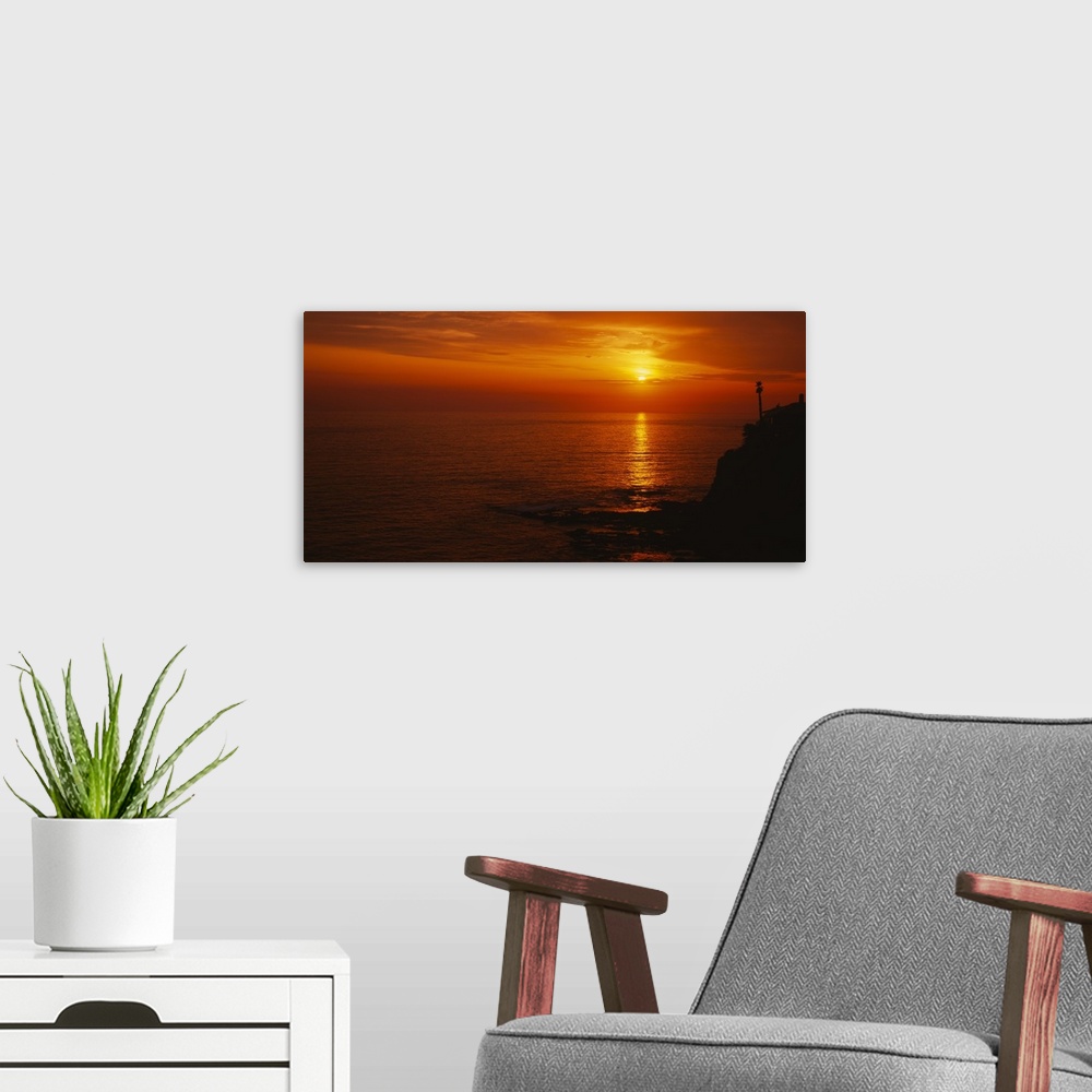 A modern room featuring Landscape, large wide angle photograph of a fiery sunset over calm waters at Laguna Beach in Cali...
