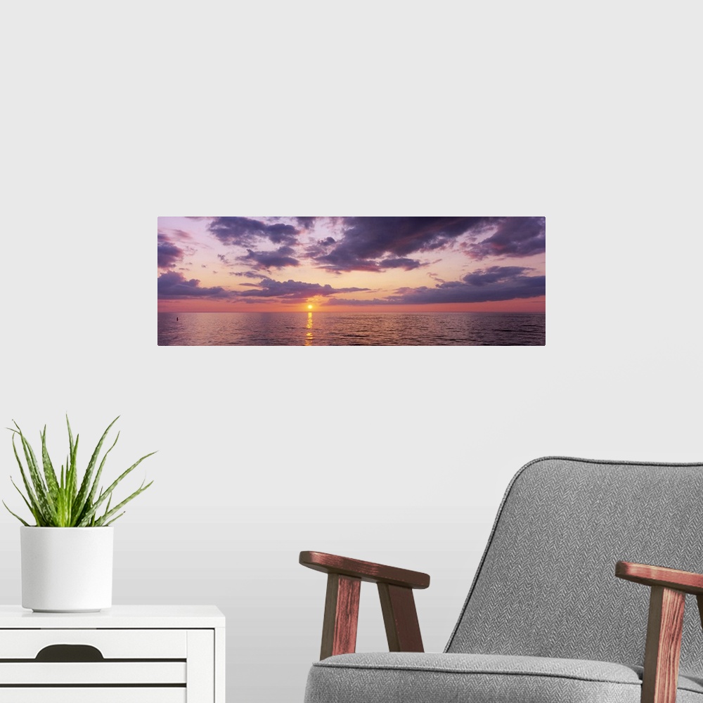 A modern room featuring Panoramic photograph taken of a sun setting over the Gulf of Mexico with warm colors throughout t...