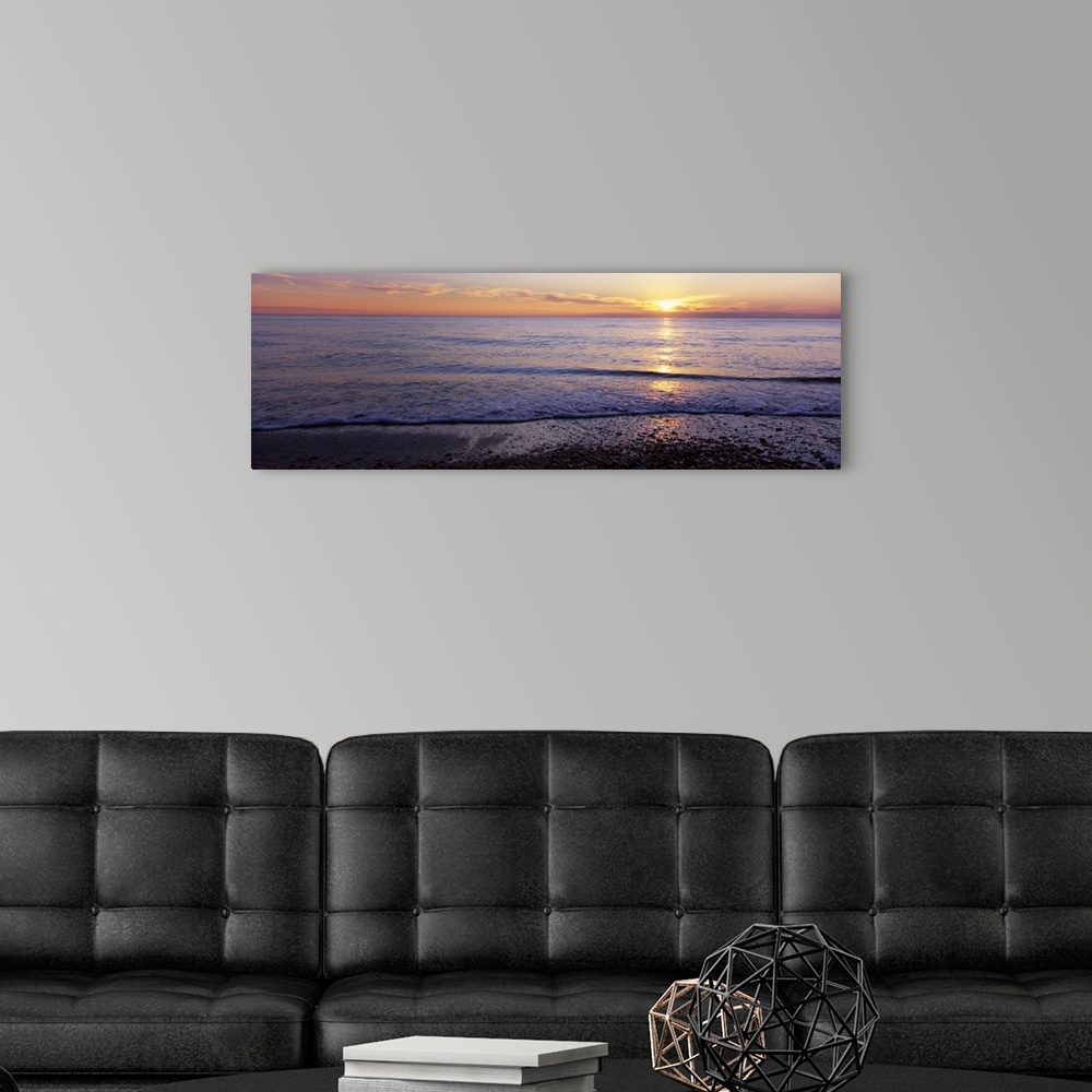 A modern room featuring This is a panoramic landscape photograph of waves softly washing up on the shore of a sandy beach.