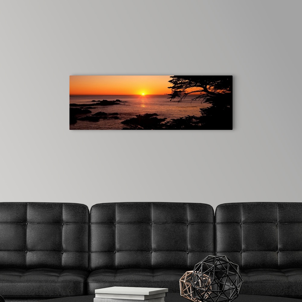 A modern room featuring Panoramic photograph of ocean with rocks emerging at the surface at dusk.  The sky is clear and t...