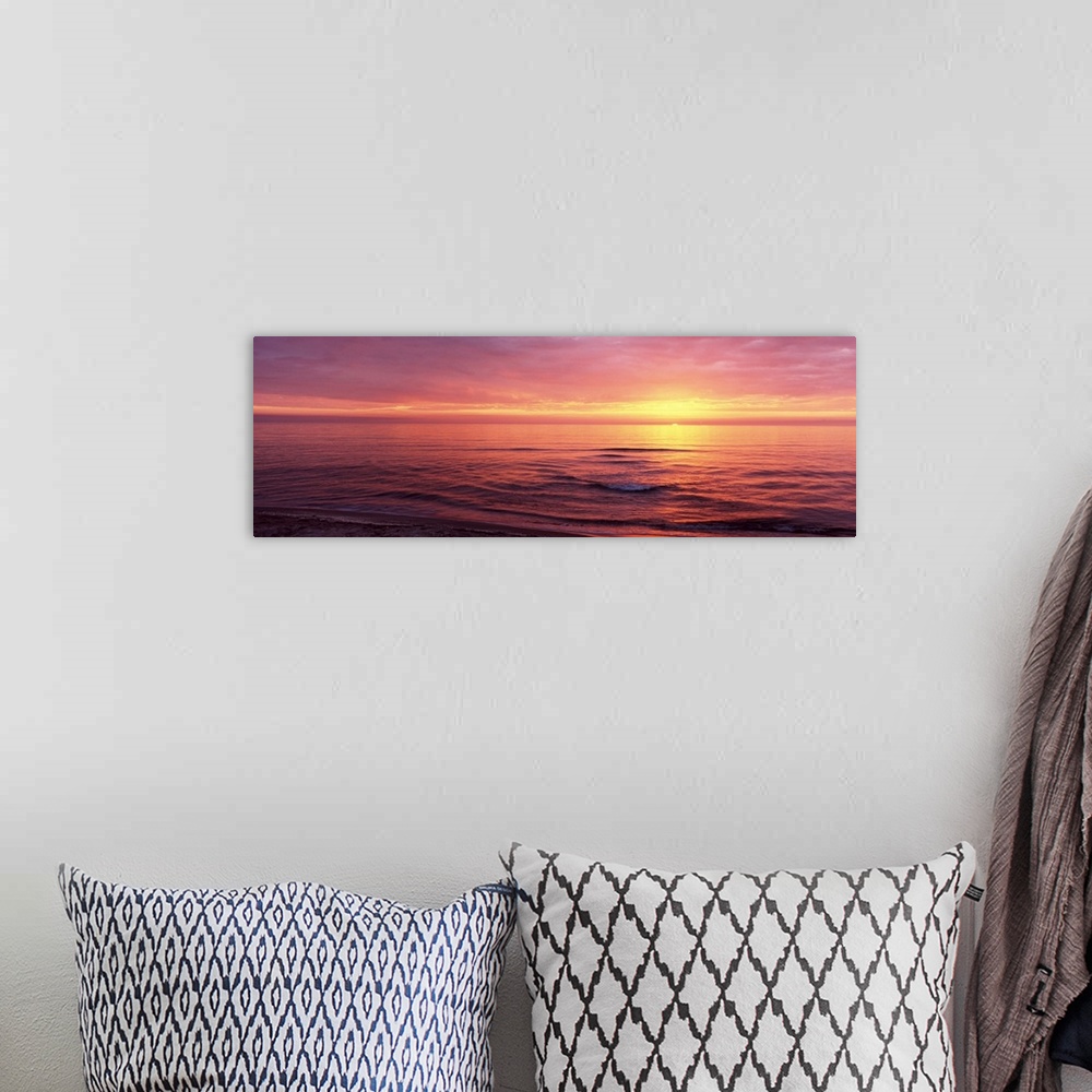 A bohemian room featuring Panoramic photograph of sun setting over ocean at dusk.