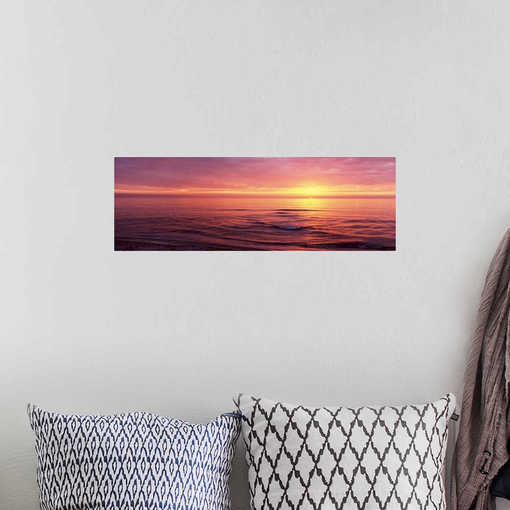 A bohemian room featuring Panoramic photograph of sun setting over ocean at dusk.