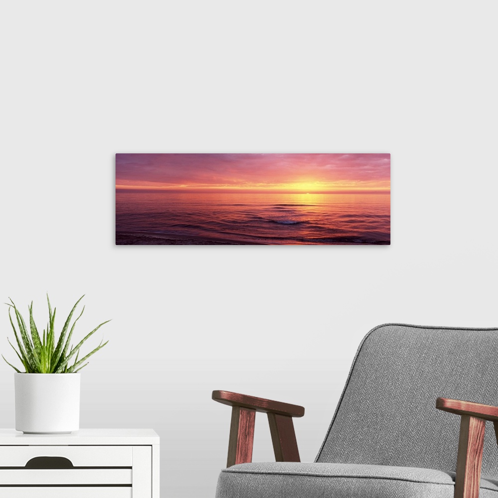 A modern room featuring Panoramic photograph of sun setting over ocean at dusk.
